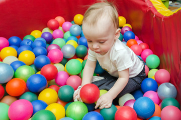 Fototapeta na wymiar little boy in a white t-shirt plays with colorful plastic balls in the playroom