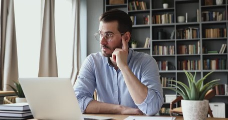 Concentrated serious businessman thinking of problem solution working on laptop. Thoughtful male programmer market analyst or software developer considering risks using computer sitting at workplace.