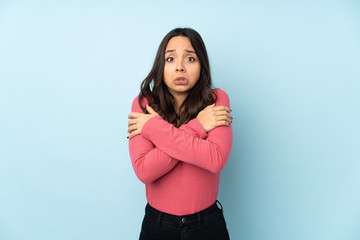 Young mixed race woman isolated on blue background freezing