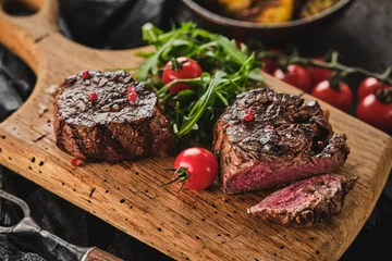  Grilled fillet steaks on wooden cutting board. Succulent thick juicy portions of grilled fillet steak served with tomatoes and roast potatoes on an old wooden board. © FoodAndPhoto