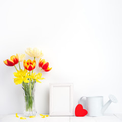Tulip flower in glass vase with picture frame place on white wooden table background against clean wall at home, close up, Mother's Day decor concept.
