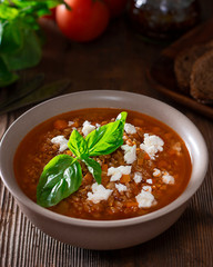 Traditional intalian vegetarian spelt soup in bowl with basil leaves and homemade cheese, surruonded by ingredients and bread on textured old wooden table. Vertical. Minestra di farro soup.