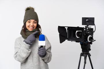 Obraz premium Reporter woman holding a microphone and reporting news over isolated white background pointing finger to the side