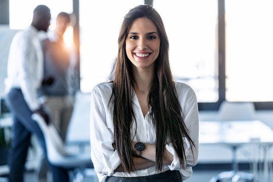 Smiling young businesswoman looking at camera while standing in the coworking space.