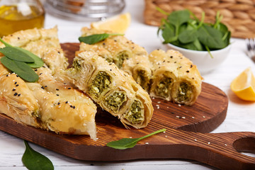 Delicious pie with spinach and feta cheese, made from filo pastry, decorated with sesame seeds. Traditional Greek pie spanakopita in a shape of roll.