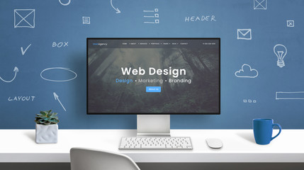 Web design studio home page on modern computer monitor. Office desk with drawings of web design...