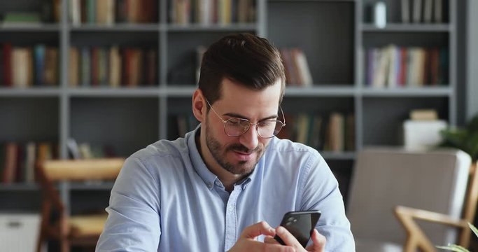 Smiling young man recording voice recognition message on speakerphone. Businessman using virtual assistant app sets reminder on smart phone at home office. Digital ai mobile assistance tech concept