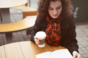 a pretty woman on the terrace of a street cafe enthusiastically reading an interesting book with a...