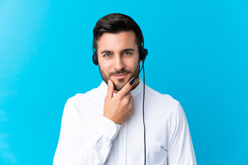 Telemarketer man working with a headset over isolated blue background laughing