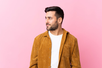 Young handsome man with beard wearing a corduroy jacket over pink background looking to the side