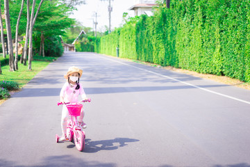 asian little girl wear a mask against PM 2.5 air pollution or disease while ride a bicycle