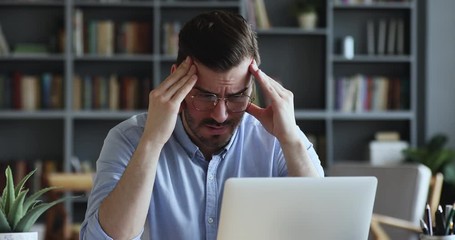 Stressed frustrated businessman wearing glasses suffering from headache at work. Exhausted tensed worker coping with migraine, emotional stress concept feeling pain sitting at office desk with laptop. - Powered by Adobe