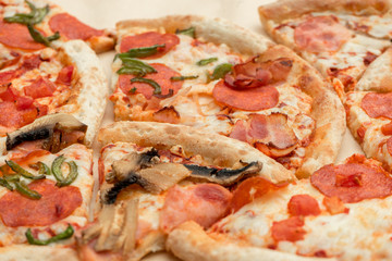 Delicious fresh pizza cut into pieces with cheese, sausage, pepperoni, bacon and mushrooms close up. High-calorie food