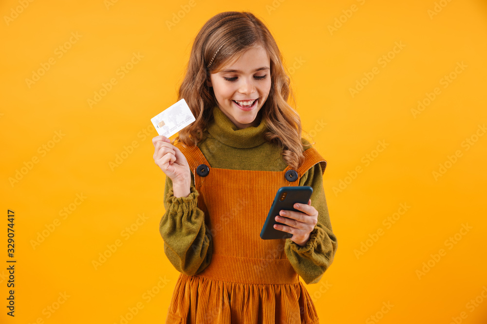 Wall mural Girl child isolated over yellow wall using mobile phone