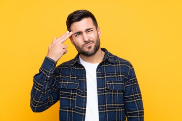 Young handsome man with beard over isolated yellow background with problems making suicide gesture