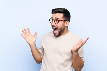 Young handsome man with beard over isolated blue background with surprise facial expression