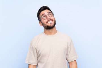 Fototapeta premium Young handsome man with beard over isolated blue background laughing and looking up