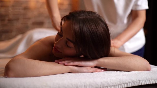 Close-up of beautiful young woman having back massage in spa salon lying on massage table, looking away. Concept of luxury professional massage. Shooting in slow motion.