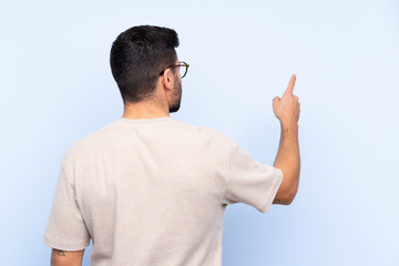 Young handsome man with beard over isolated blue background pointing back with the index finger