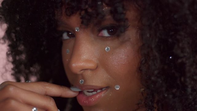 mixed race model covered by crystals makeup with shiny skin bite her finger watching to the camera