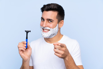 Young handsome man shaving his beard over isolated background points finger at you with a confident...