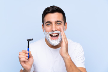 Young handsome man shaving his beard over isolated background shouting with mouth wide open