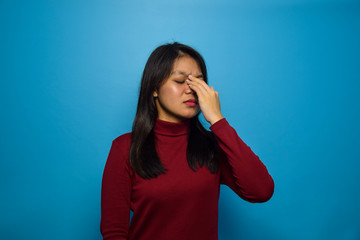 Portrait of Young beautiful asian women with blue isolated background, rubbing nose and eyes feeling fatigue and headache, stress and frustration gesture