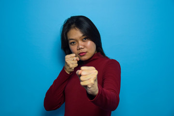 Portrait of Young beautiful asian women with blue isolated background, Punching fist to fight, Fight concept gesture