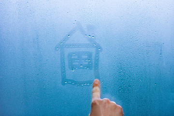 hand draws a house on a glass window with drops background