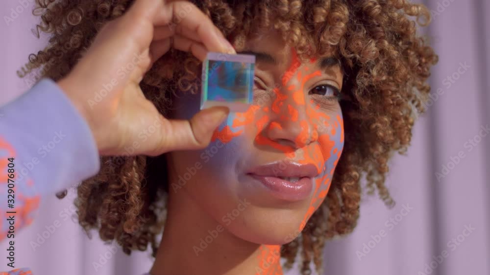 Wall mural Closeup portrait of mixed race woman with neon art makeup on face With cristal cube in front of her eye. New beauty new identity concept