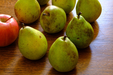 Still life of backlit pears on antique wood table.