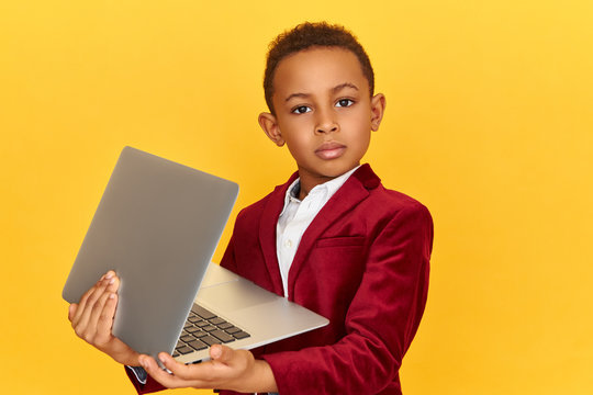 Technology, electronic gadgets and devices concept. Studio image of confident dark skinned little boy posing isolated with laptop on his hands, using wireless high speed internet connection