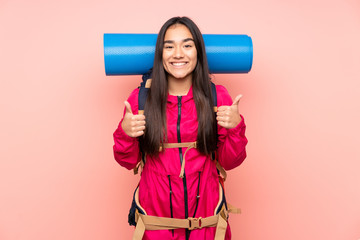 Young mountaineer Indian girl with a big backpack isolated on pink background giving a thumbs up gesture