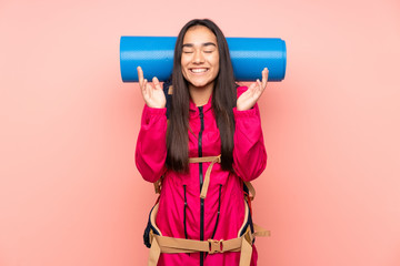 Young mountaineer Indian girl with a big backpack isolated on pink background laughing