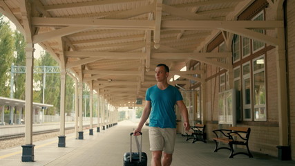 Young Man is Traveling and Walking on Vintage Railroad Station Platform with Suitcase