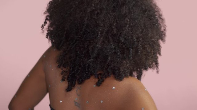 Mixed race black woman with curly hair covered by crystal makeup on pink background in studio dancing in slow motion from 60 fps