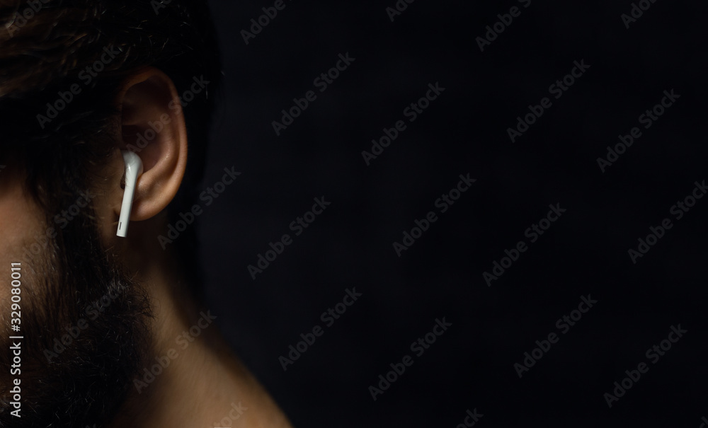 Canvas Prints close-up of wireless earphone in male ear on background of black color with copy space.