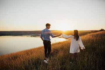 Rear view of a couple walking and enjoying sunset together. Couple walking on the beach. Girl are dressed in white dress and boy in elegant stylish clothes.