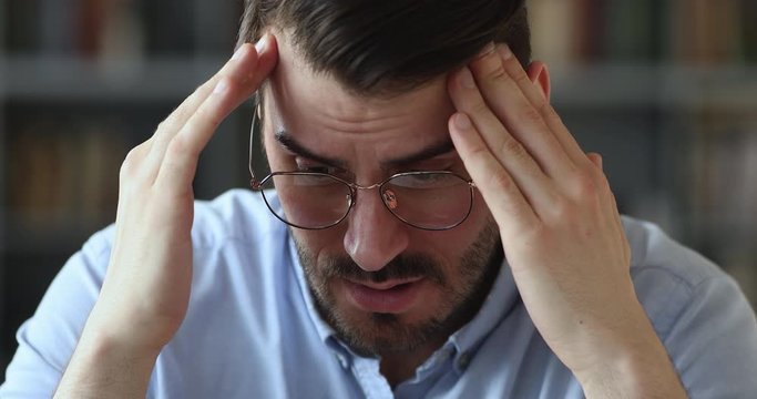 Sick stressed 30s man feeling pressure and strong headache pain. Upset worried young adult businessman suffering from anxiety or mental stress, having panic attack, migraine concept. Close up view