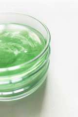 Transparent green shampoo or facial cleaner in glass petri dish on white background with selective focus, above. Concept natural organic cosmetic