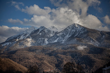 Mountain landscape in early spring. The fog slides from the mountains. Snow peaks. Ski resort. Beautiful highland background. Wide view of the mountain range. The calm of northern nature.