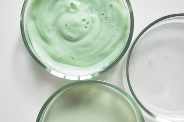 Close-up glass petri dishes with shampoo, shower gel and serum with copy space, above