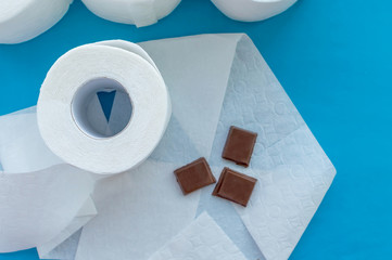 Concept. Chocolate on toilet paper next to a roll of toilet paper on a blue background. The view from the top.