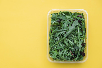 Fresh leaves of arugula, lettuce, spinach, beets for salad in a plastic plate on a yellow background. Top view. Copy, empty space for text