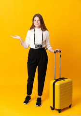 Full body of traveler teenager girl with suitcase over isolated yellow background holding copyspace imaginary on the palm