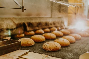 Zelfklevend Fotobehang Verse broodjes uit de oven. Transportband met brood. Brood bakken. Workshop voor de productie van brood. Wit brood in de oven. Warme broodjes. Banketbakkerij © Roman