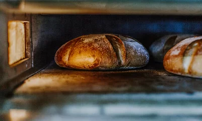 Zelfklevend Fotobehang Verse broodjes uit de oven. Transportband met brood. Brood bakken. Workshop voor de productie van brood. Wit brood in de oven. Warme broodjes. Banketbakkerij. © Roman