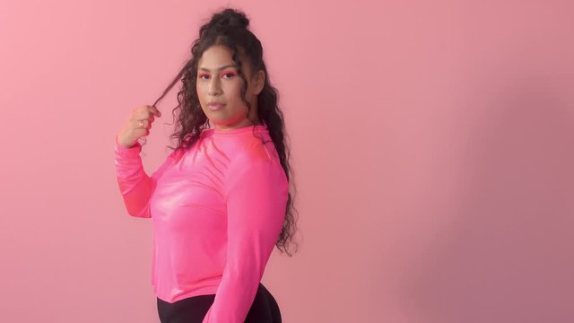 Young plus size mixed race woman with curly hair wears a bright neon makeup in pink studio New beauty without norms concept