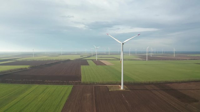 Aerial fly around wind turbines across spring agricultural field. Clean and Renewable Wind Power Farm in Motion. Green energy, sustainable alternative electricity, no pollution environment.