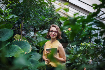 Young woman with tablet standing in botanical garden. Copy space.